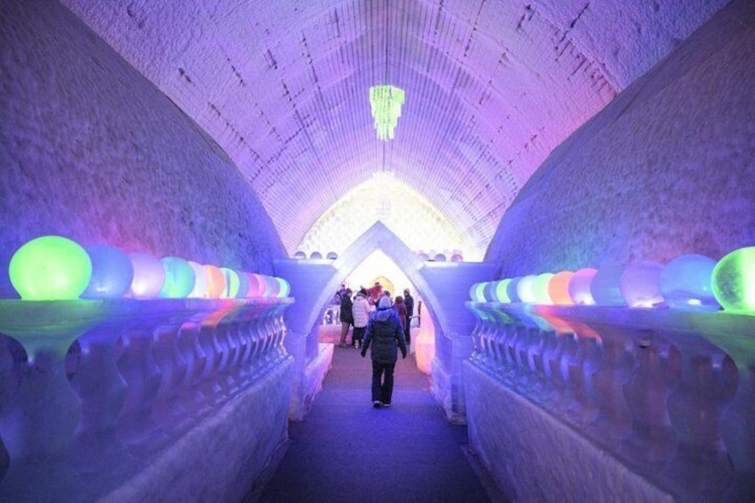 An ice tunnel with colorful illuminated spheres and a crowd of people walking through. 2