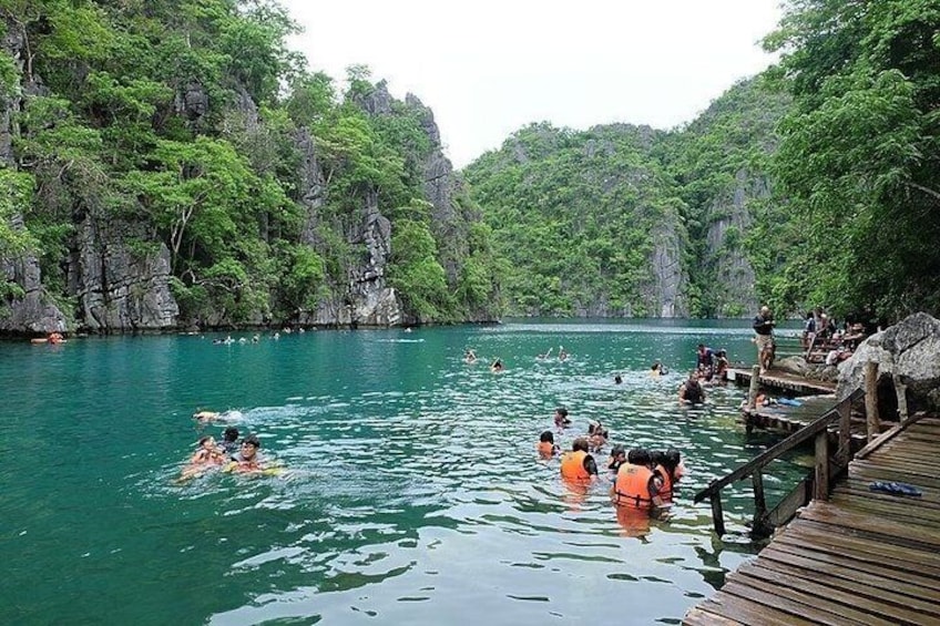 A group of people swimming and floating on a turquoise lake surrounded by lush greenery and rocky cliffs. 3