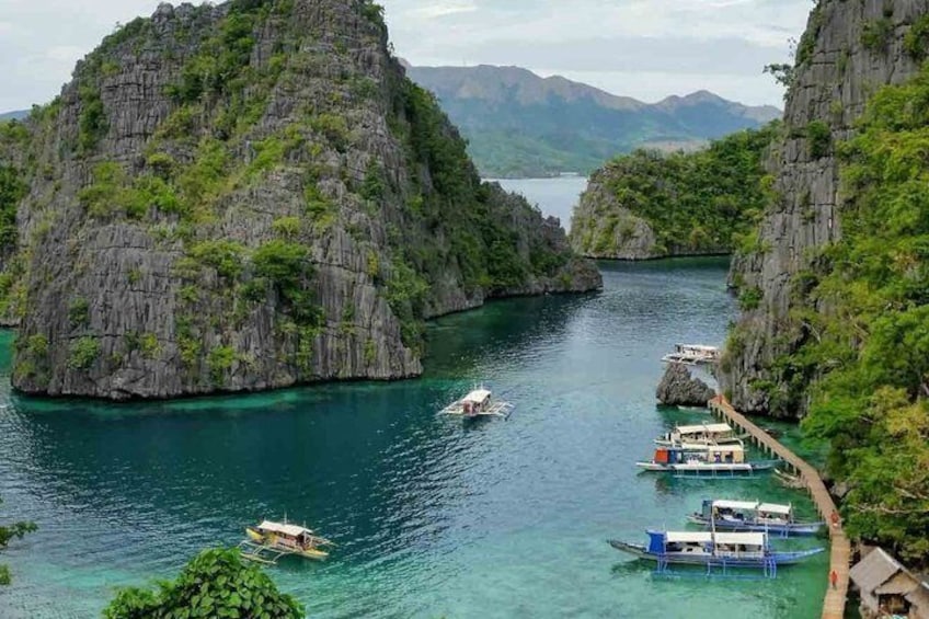 A coastal scene with boats docked along a pier, surrounded by rocky cliffs and lush greenery. 1