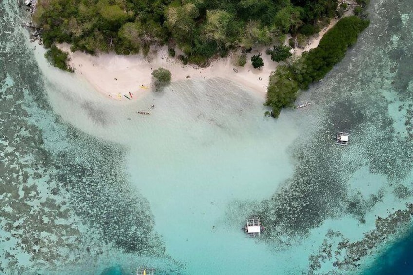 An aerial view of a beach with clear turquoise waters, a sandy shore, and a small boat anchored near the shore. 4