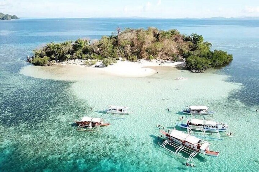 A clear turquoise sea with boats anchored near a small island with dense vegetation. 5