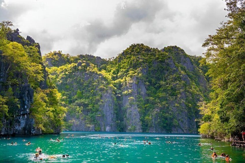 A turquoise sea with people swimming and a forested mountain in the background. 2