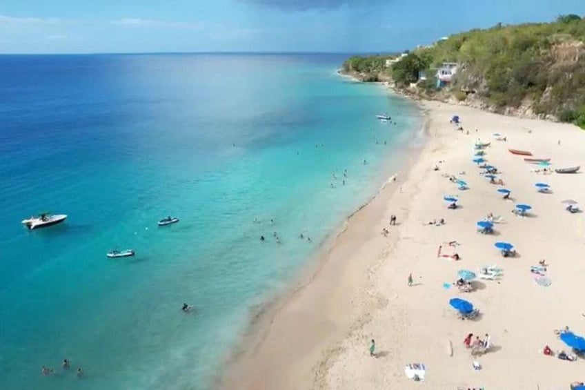 A beach with clear turquoise water, boats, and people. 3