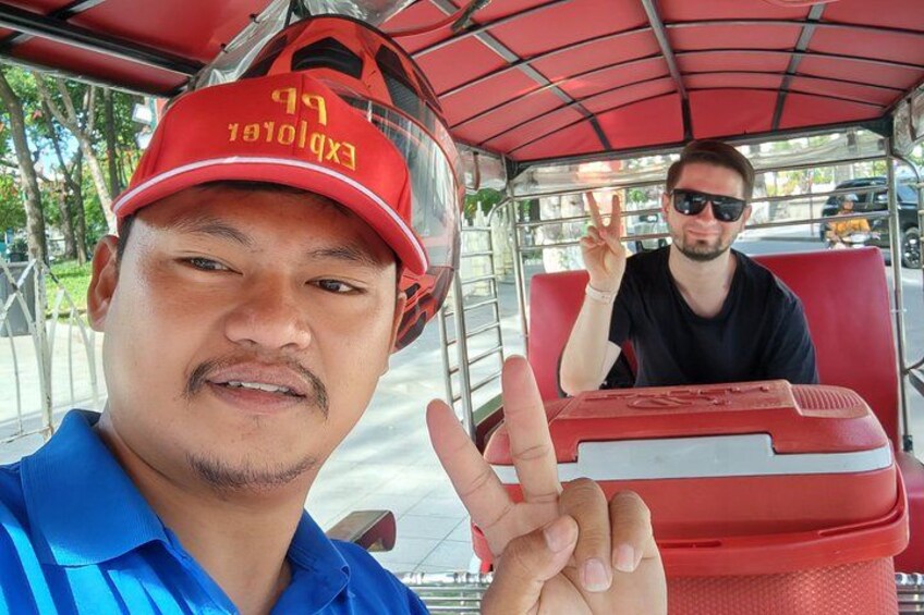 Two people in a red vehicle, one wearing a red cap with text, and the other making a peace sign. 5