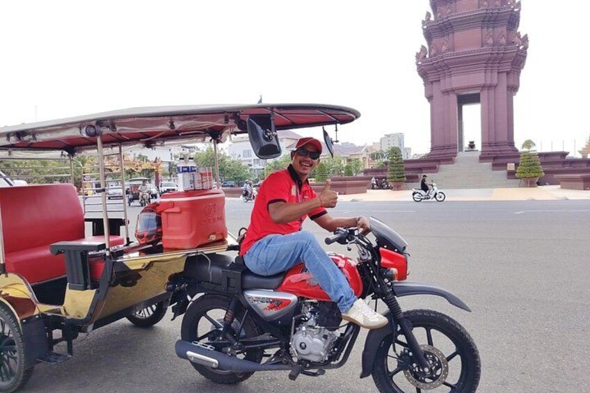 A person on a motorcycle with a trailer, in front of a large monument. 4
