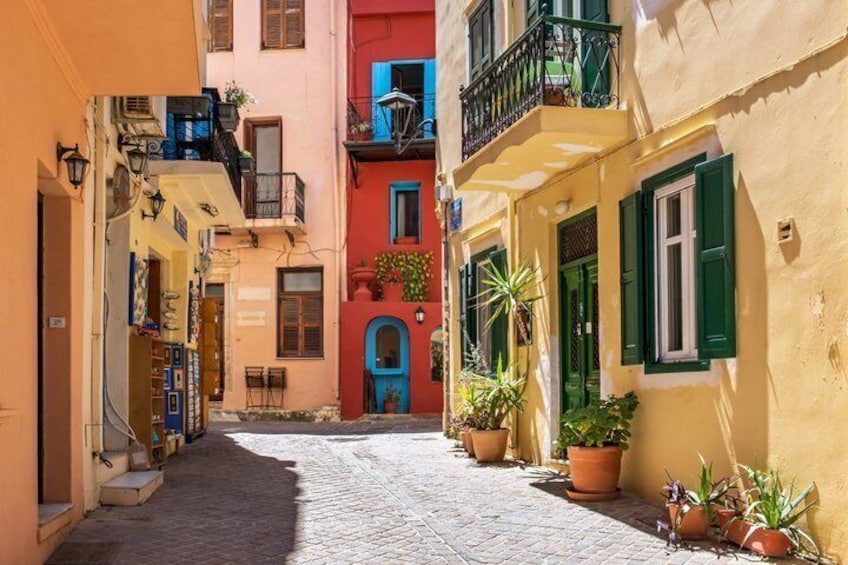 A narrow cobblestone street flanked by colorful buildings with balconies and potted plants. 2