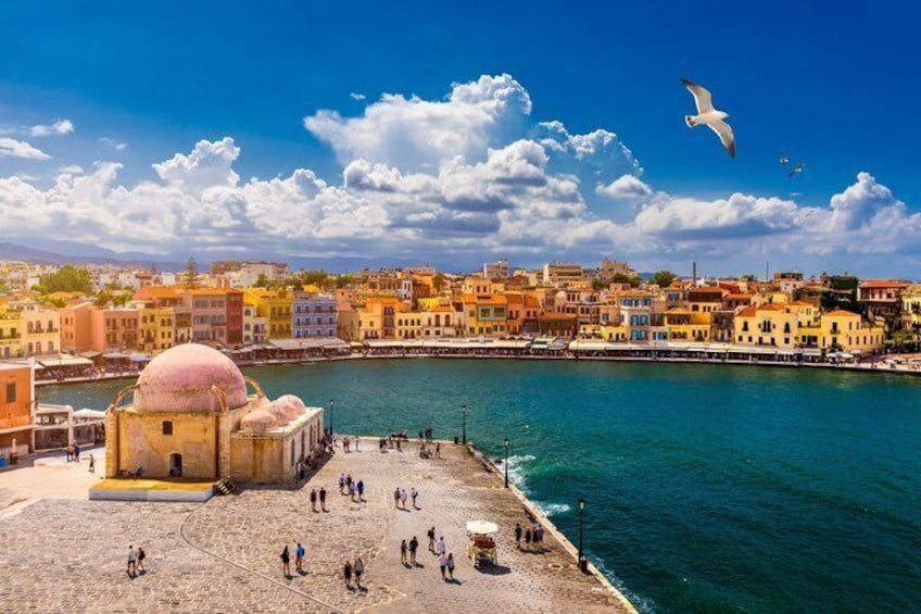 A coastal cityscape with a prominent pink-domed building, a bustling waterfront promenade, and a clear blue sky. 5