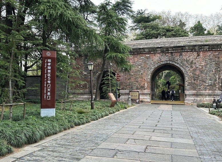 A stone pathway leading to an arched entrance with a signboard and a lamppost. 1