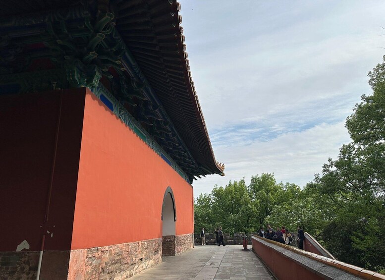 A traditional building with a red facade and ornate roof, a stone pathway, and a tree-lined area with people in the distance. 2