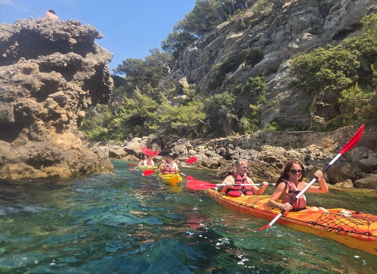 A group kayaking on clear water with rocky cliffs and greenery in the background. 2