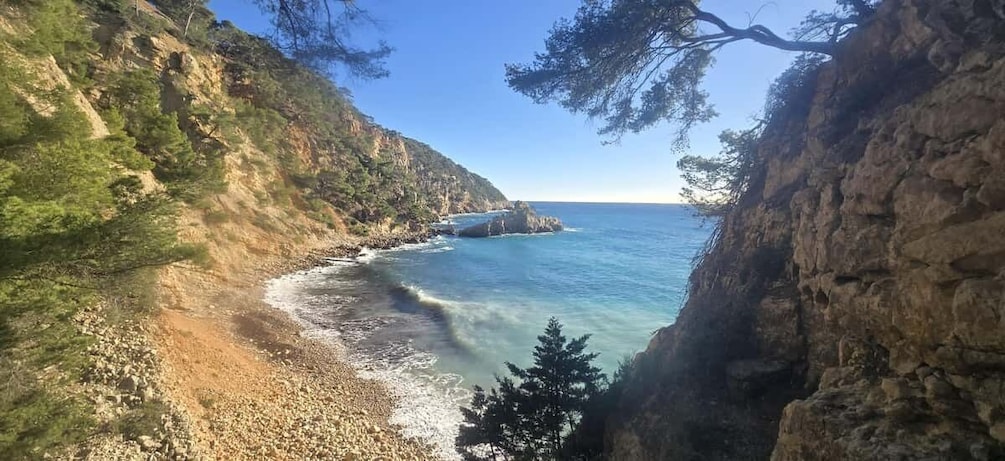 A coastal landscape with rocky cliffs, a pebble beach, and clear blue sea. 1