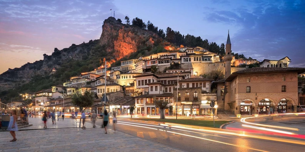 A historic town with buildings on a hillside, a prominent church, and a roundabout with light trails. 4