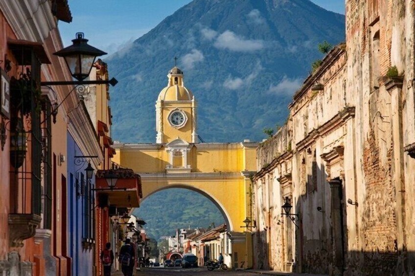 A street with a yellow arch bridge, a clock tower, and a mountain in the background. 3