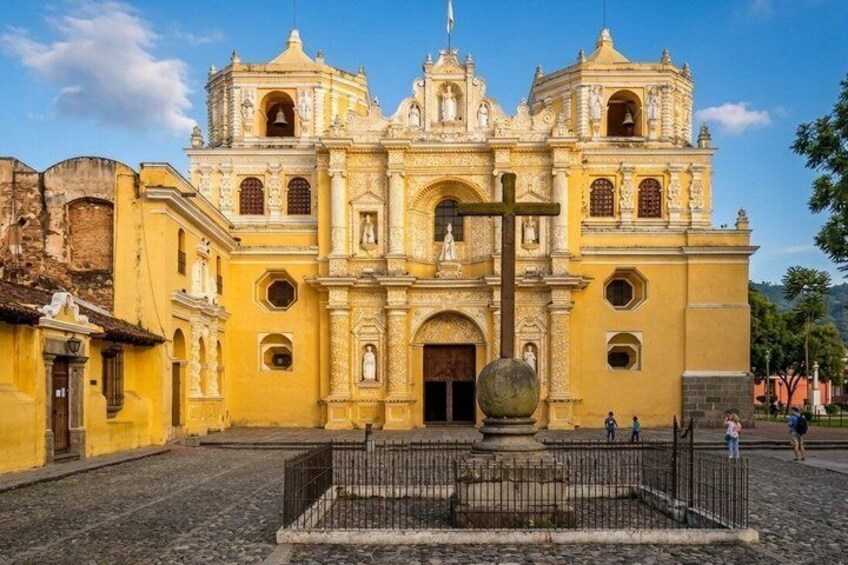 A historic yellow church with a large cross in front. 2