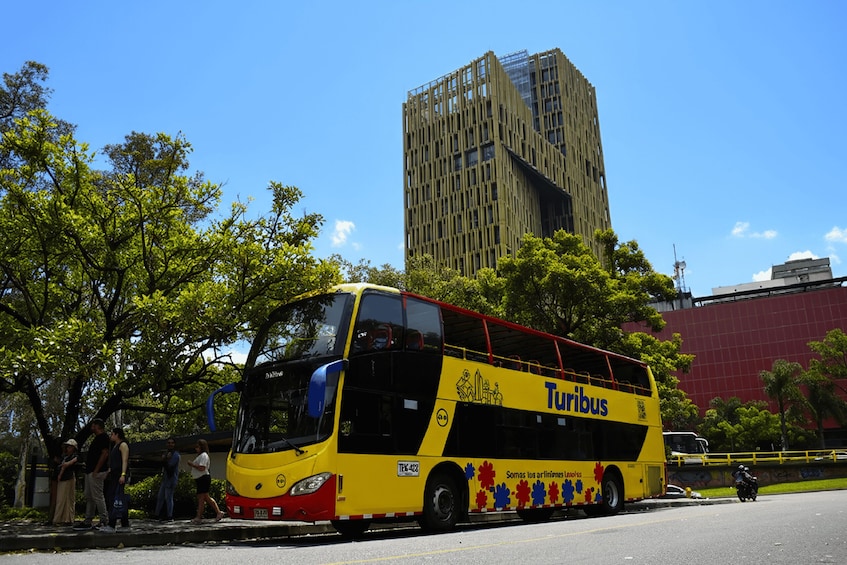 A yellow double-decker bus with 'Turibus' written on it, parked on a street with trees and a tall building in the background. 1