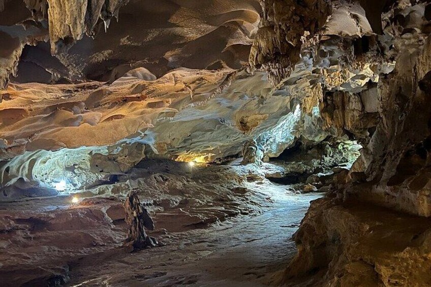 Una cueva con estalactitas y estalagmitas, un arroyo y una persona de pie en el centro. 3