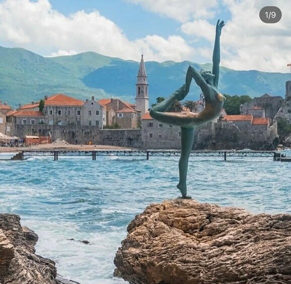 A person performing a handstand on a rock by the sea with historic buildings and a tower in the background. 1