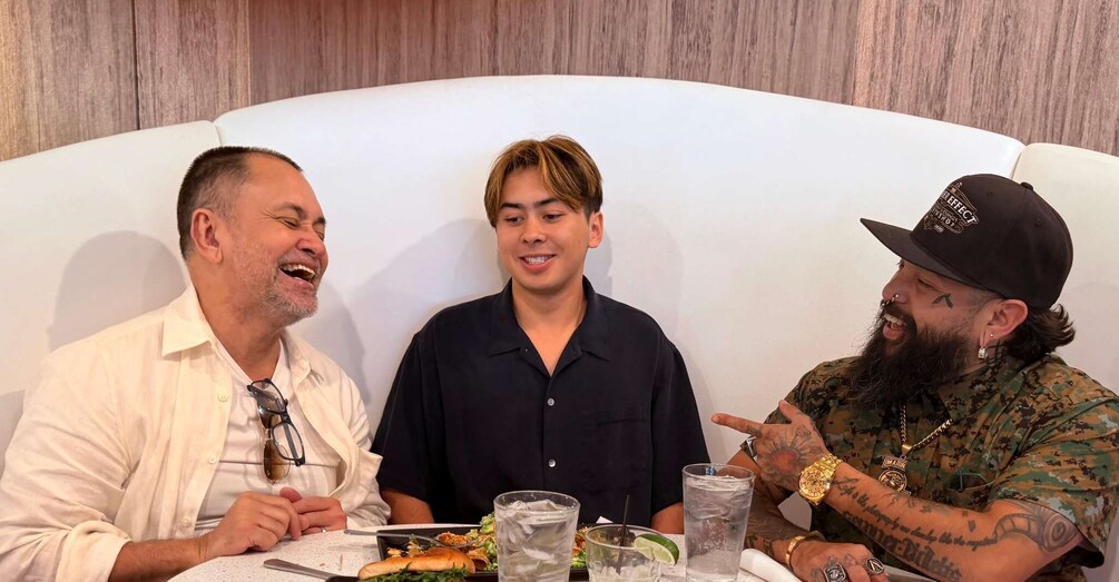 Three people seated at a table with food and drinks. 1