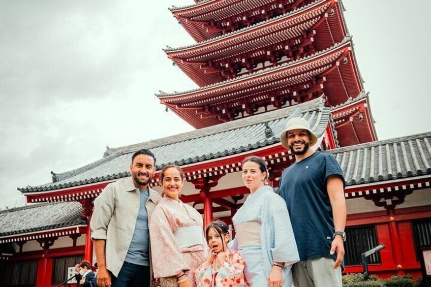 A group of people standing in front of a traditional red and grey pagoda-style building. 1