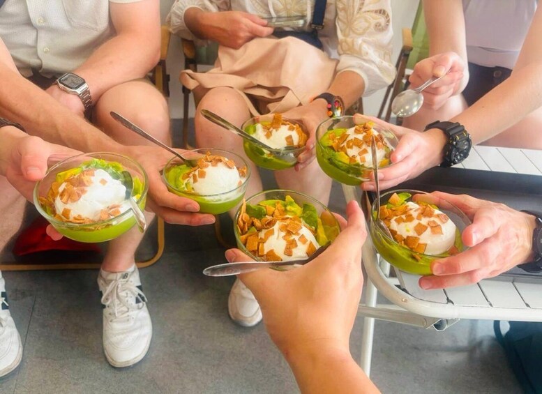 A group of people holding bowls of dessert with a green base, white topping, and crumbled topping. 1