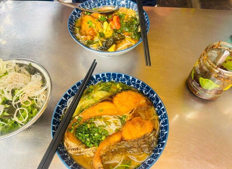 Two bowls of soup with chopsticks, a jar of sauce, and a bowl of salad. 2