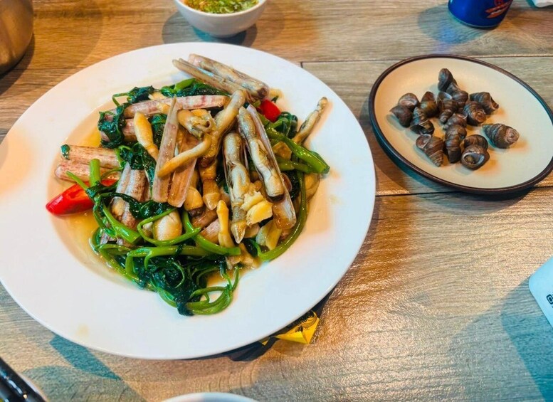 A plate of stir-fried vegetables and meat, a bowl of green sauce, and a plate of small round items, possibly nuts, on a wooden table. 3