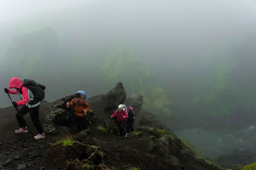 Hikers on a foggy mountain trail with rocky terrain and moss-covered rocks. 2