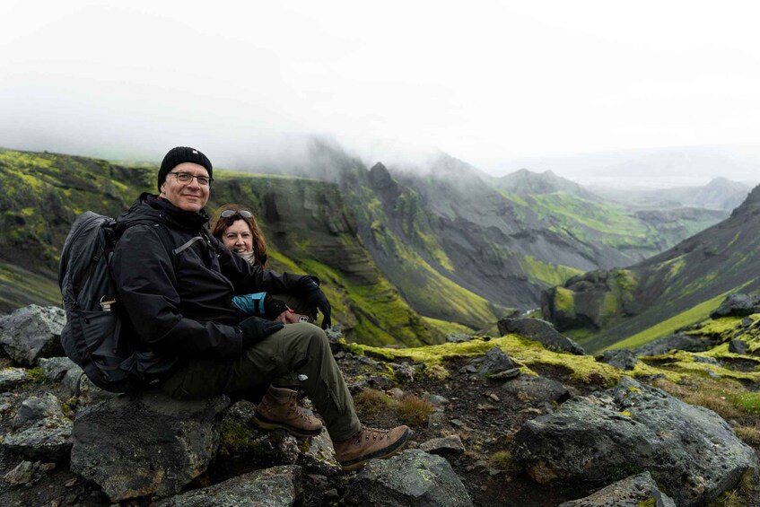 Two people sitting on a rocky outcrop with a mountainous landscape in the background. 3