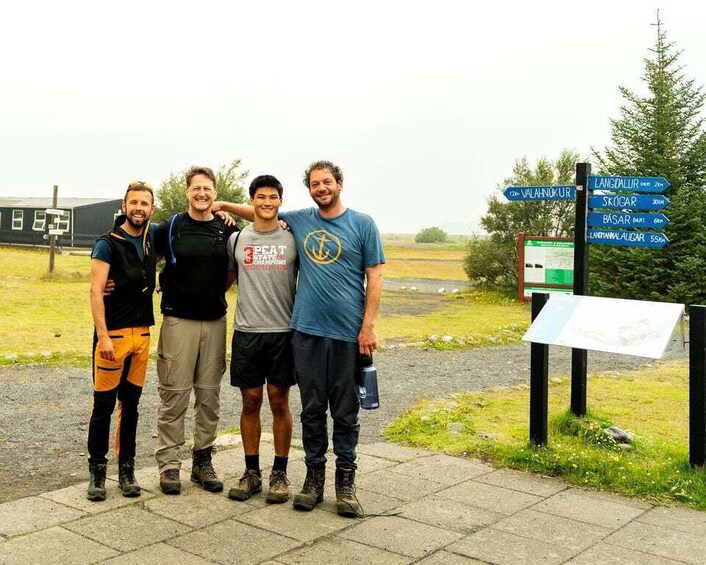 Four people standing in front of a signpost with directions to various locations. 5