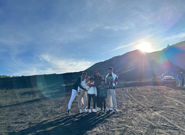 A group of people standing on a dirt road with a mountain in the background and a vehicle parked nearby. 5