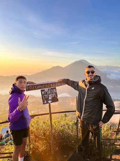 Two people standing on a mountain trail with a sign that reads 'Welcome to Mt. Batur 1,717 MDPL.' 2