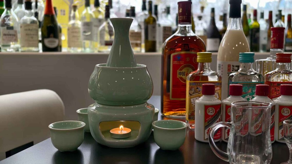 A table with a green ceramic tea set, a candle, and various bottles of alcohol. 3