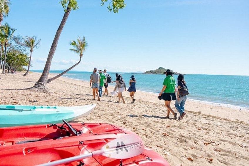 A beach with people walking, palm trees, and kayaks. 5