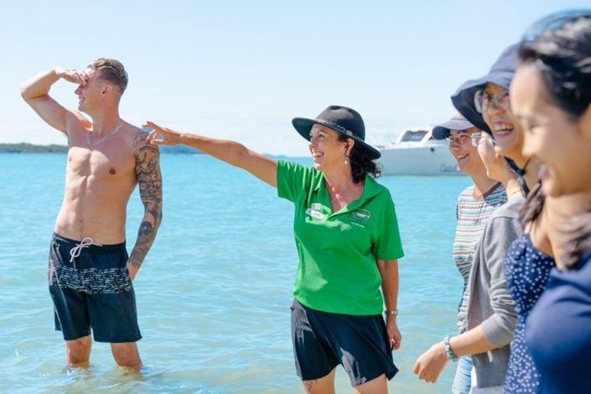 A group of people standing in shallow water near a boat, with a clear sky and calm sea. 3