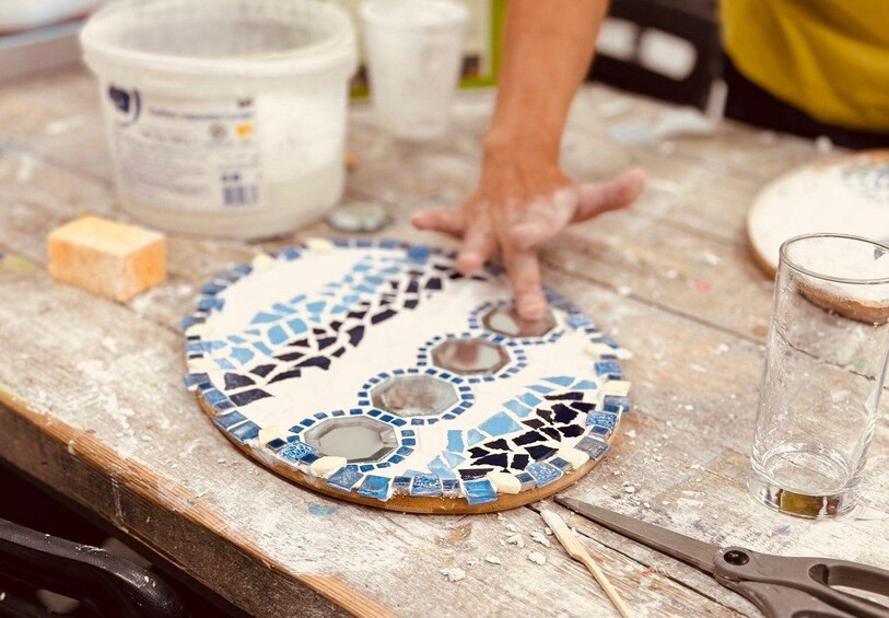 A mosaic tile with a hand placing pieces on a workbench. 3