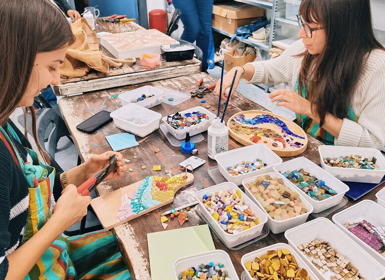 A workshop with people engaged in mosaic art, surrounded by various colored tiles and tools. 1