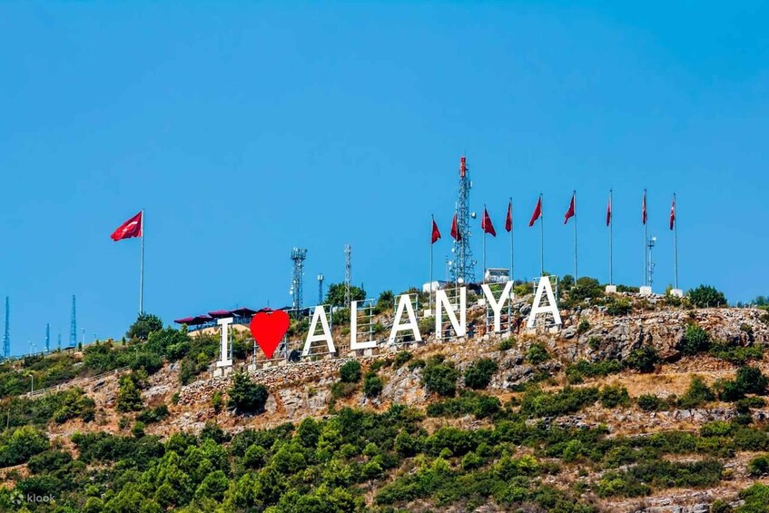Kukkulan päällä on sana »ALANYA» ja useita punaisia lippuja. 2