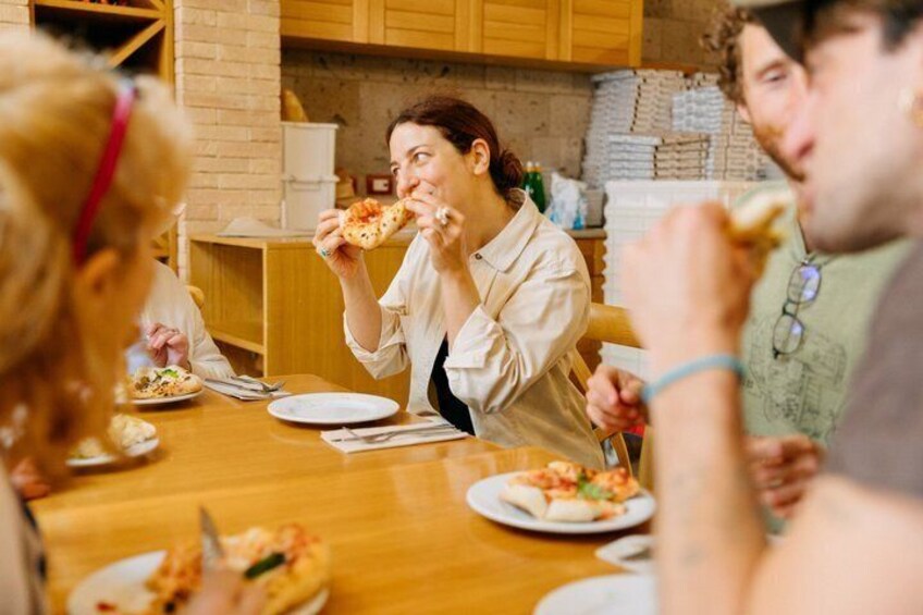 People eating pizza at a wooden table in a kitchen. 4