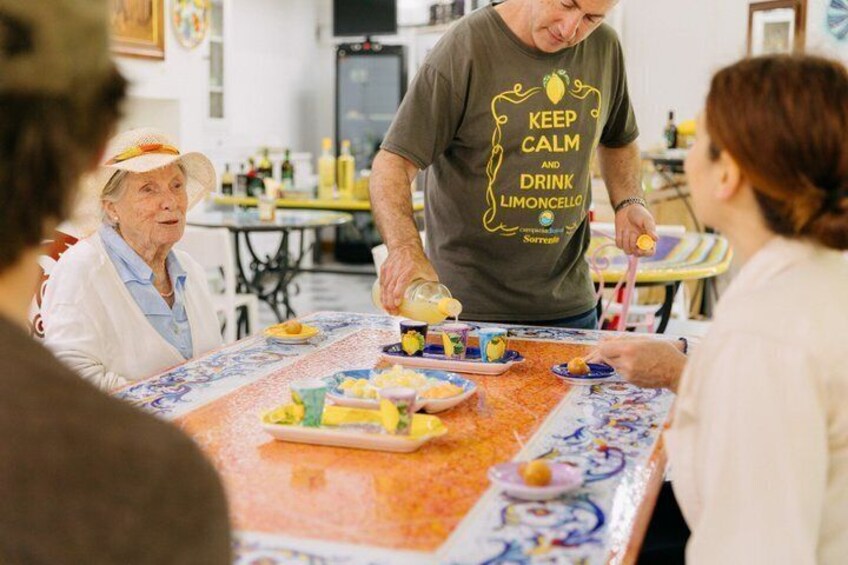 A person serving food at a table with a colorful tablecloth, surrounded by seated individuals. 3