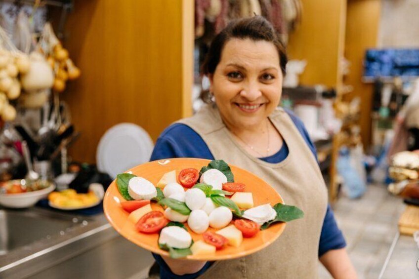 A person holding a plate of Caprese salad with tomatoes, mozzarella, and basil. 1