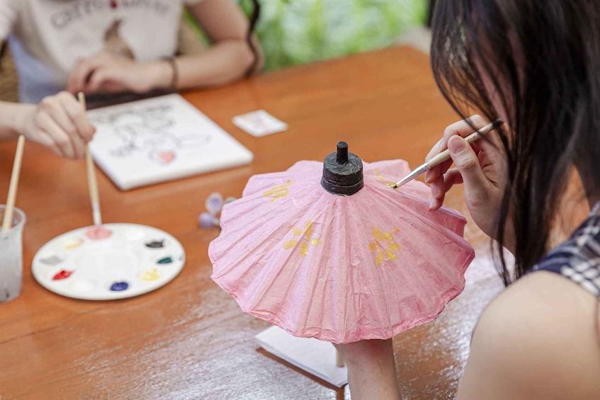 A person painting a pink paper umbrella with yellow flowers. 5