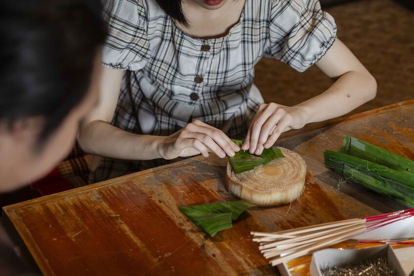 A person wrapping food in banana leaves on a wooden table. 4
