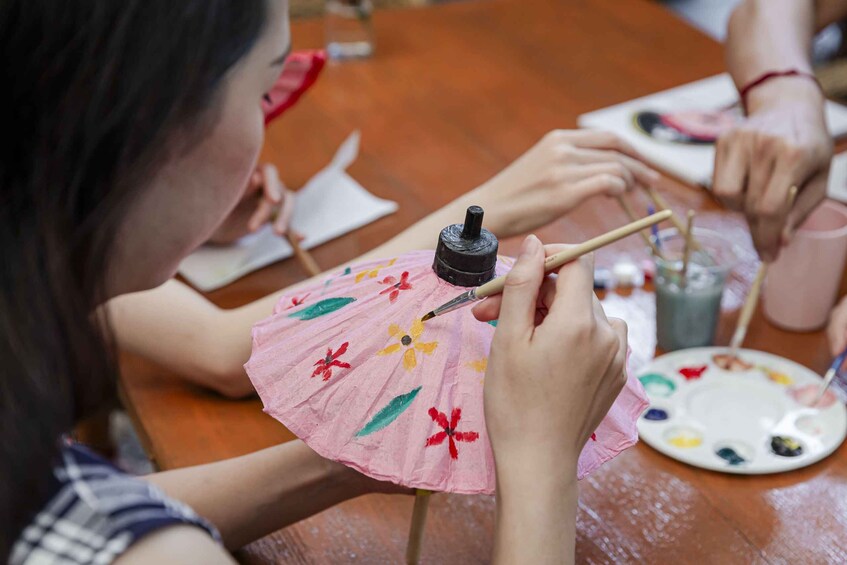 A person painting a pink fan with floral designs. 3