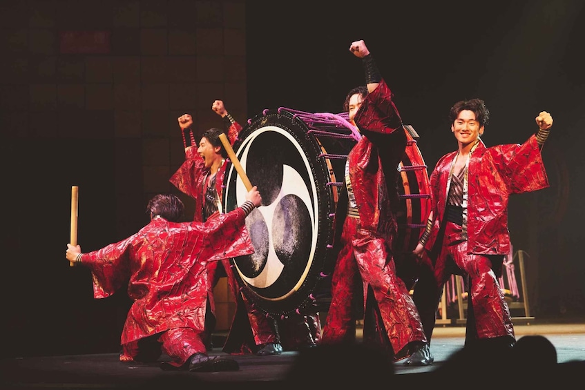 A group of performers in red costumes on stage with a drum set. 1