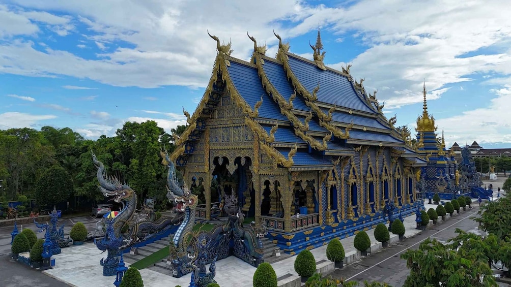 A temple with intricate blue and gold decorations, a large dragon statue, and a clear sky. 3