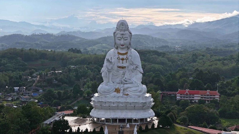 A large white statue of a seated figure with a lotus base, surrounded by lush greenery and mountains in the background. 5