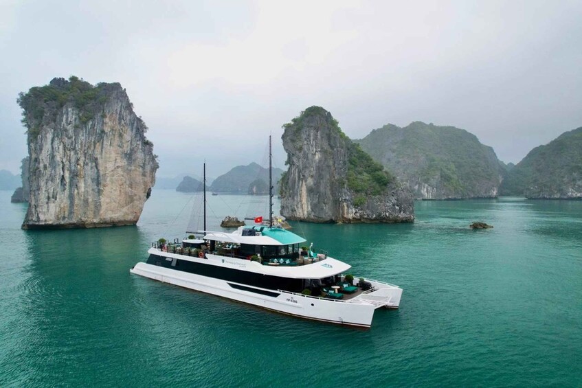 A white boat with a green roof sailing between two large limestone islands in a turquoise sea. 1