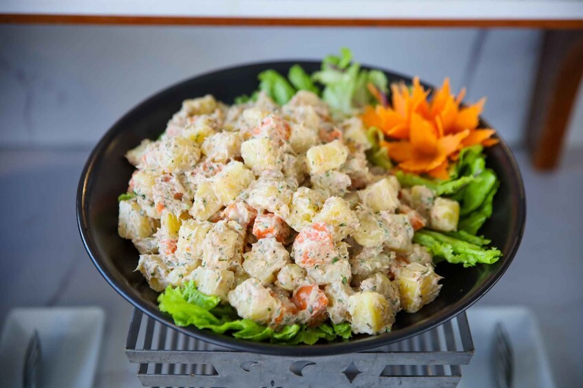 A bowl of potato salad with carrots and herbs, garnished with lettuce and a carrot flower, on a metal stand. 4