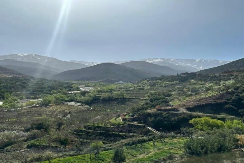 Un paisaje montañoso con un río, vegetación y picos nevados a lo lejos. 1