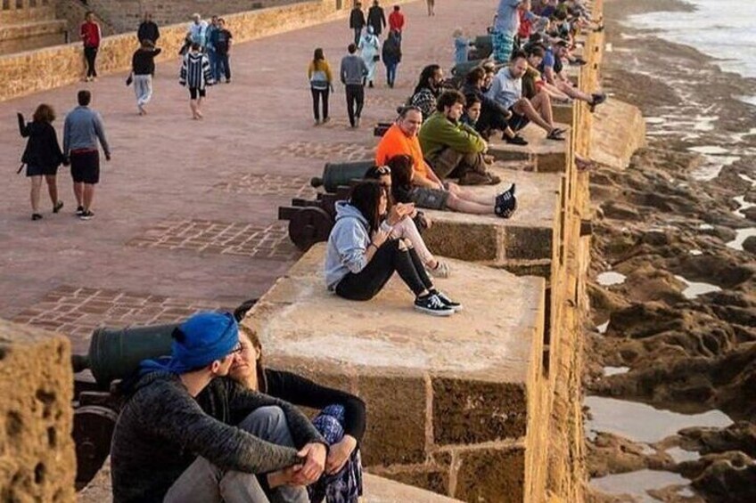 People sitting and walking on a stone pathway by the sea. 4